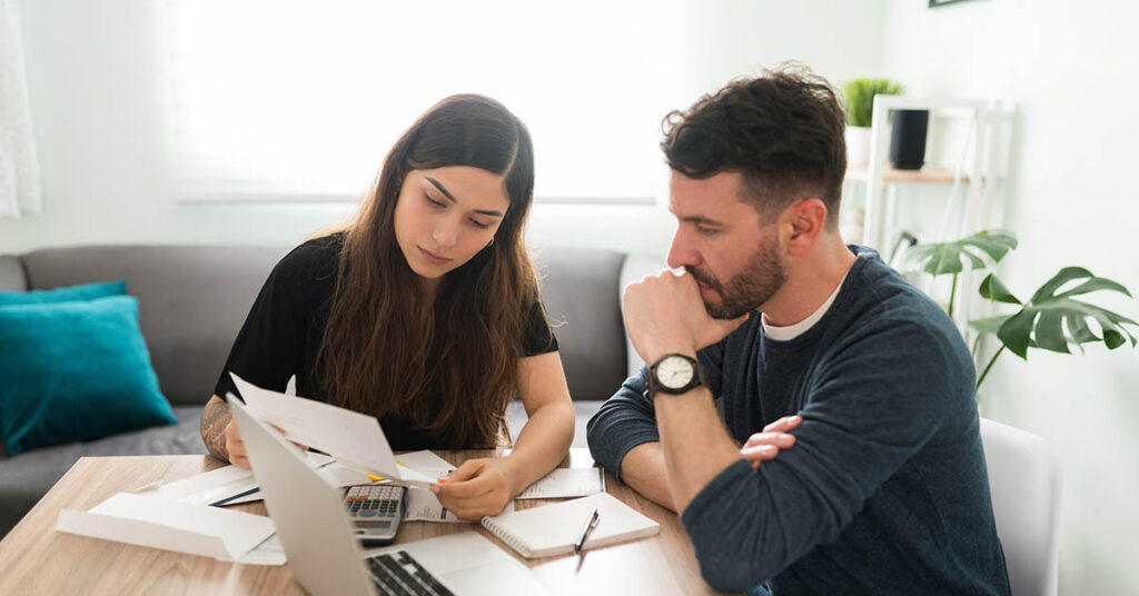 Stressed couple reviewing HOA lien documents and bills at home